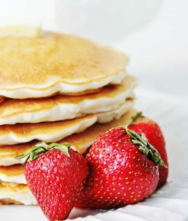 a stack of golden pancakes accompanied by fresh, ripe strawberries on a white, textured background.